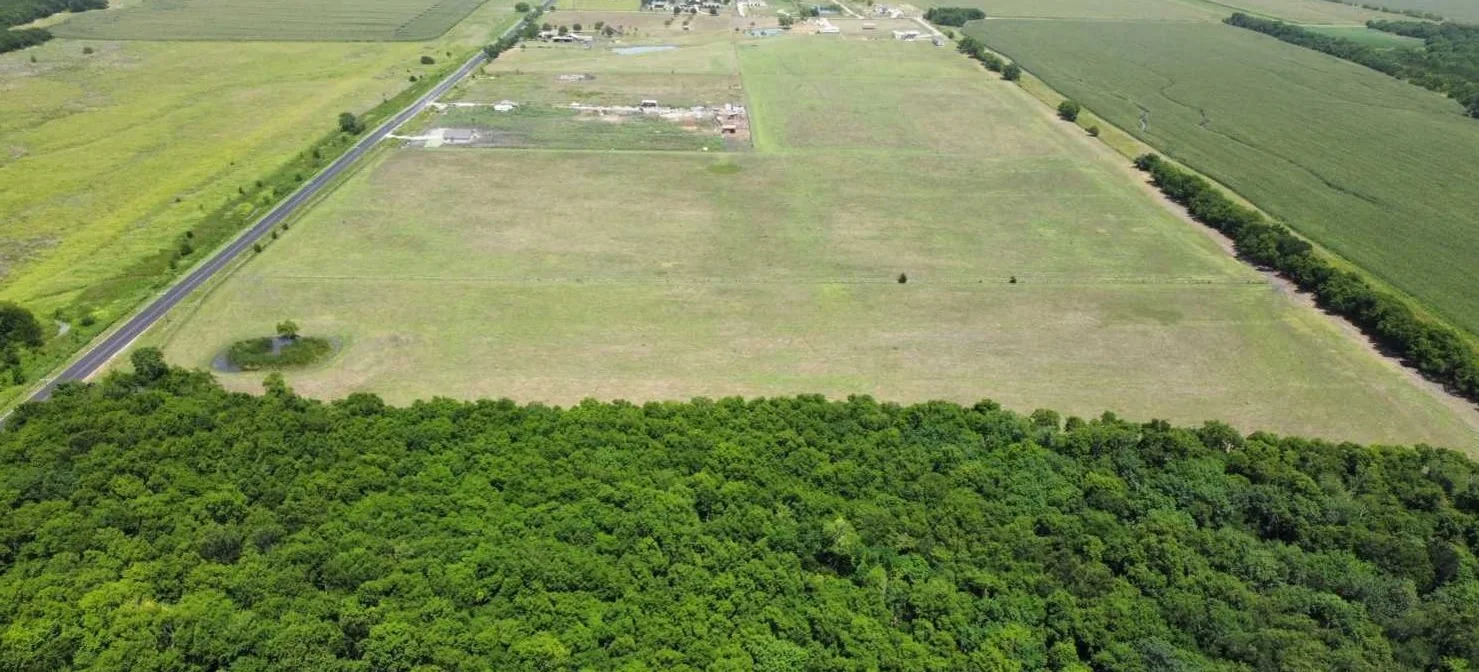 Aerial view across the 40-acre parcel: county road frontage at left, a stock pond, open pasture, and the wooded southern boundary